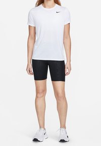 Nike kortärmad vit skjorta, åtsittande svarta shorts med texturerat mönster, vita och svarta sportskor, neutral bakgrund.