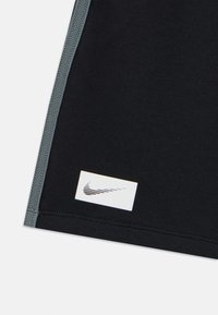 Black athletic shirt featuring grey stitching and a white Nike logo patch near the hem. Smooth texture and fitted design.