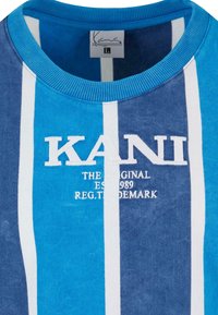 Mėlynas ir tamsiai mėlynas dryžuotas megztinis su guma apykakle. Ant megztinio yra balta siuvinėta "KANI" logo, o žemiau - papildomas tekstas. Maloni tekstūra.