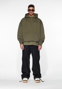 Olive green hooded sweatshirt with a front pocket, paired with black cargo pants featuring multiple pockets, and white sneakers with orange soles.