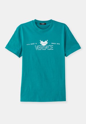 T-shirt en coton turquoise avec col rond, manches courtes et texte imprimé blanc, incluant "VERSACE" et un motif de flamme décoratif.