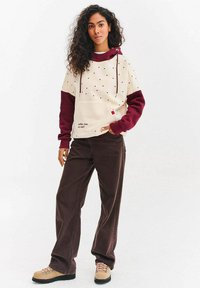 Bluza w kremowo-bordowe bloki kolorystyczne z groszkami, kapturem ze sznurkiem, przednią kieszenią i detalem z napisem. Połączona z brązowymi sztruksowymi spodniami.