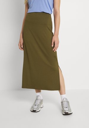 Jupe longueur genou de couleur vert olive, taille ajustée avec des fentes latérales. Assortie à des chaussures de sport argentées et des chaussettes blanches. Texture de tissu lisse.