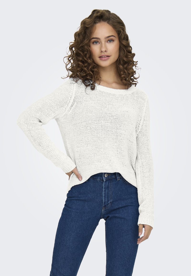 Maglione bianco lavorato a maglia con taglio ampio, scollo largo e maniche lunghe. Abbinato a jeans di denim scuro a vita alta. Tessuto strutturato.