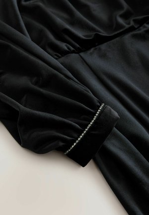 Schwarzes Samtkleid mit langen Ärmeln, das an der Taille geraffte Details und verzierte Manschetten mit einer Reihe von kleinen, glänzenden Akzenten aufweist.