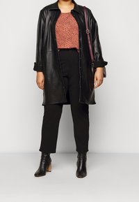 Černá kožená dlouhá košile s bundou přes červený top s puntíky, kombinováno s černými přiléhavými kalhotami a černými vysokými kotníkovými botami. Burgundská kabelka na rameno.