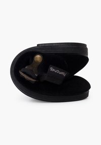 Scarpa nera slip-on realizzata in materiale morbido e testurizzato, con una forma curva e una chiusura a fibbia metallica. Accentuata da un'etichetta in tessuto con logo.