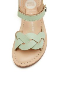 Sandal in pelle verde chiaro con design della fascia intrecciata, soletta beige con dettagli di cucitura e cinturino alla caviglia regolabile.