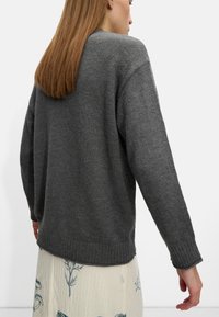 Szary sweter dzianinowy o luźnym kroju, z prążkowanymi mankietami i dołem. Widoczna faktura, okrągły dekolt oraz lekko oversize'owy fason.
