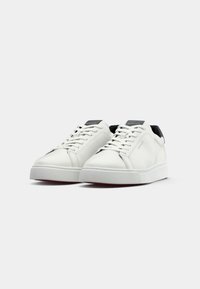 Adidași din piele albă cu un finisaj neted, vârf rotund și accente negre la călcâi. Încălțare cu șireturi și talpă plată din cauciuc.