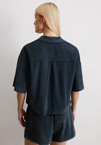 Dark navy short-sleeve shirt in soft fabric, featuring a collar, back vent, and relaxed fit, paired with matching shorts.