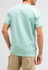 Mint green short-sleeve t-shirt with a rounded neckline and a smooth texture, worn with light beige cargo shorts.