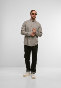 Hemd mit Knopfleiste in einem karierten Muster, hellgrau und dunklen Tönen, kombiniert mit schwarzen Jeans und hellen Sneakers. Plastikgestell-Sonnenbrille getragen.