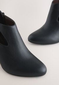 Black leather ankle boots with a pointed toe, cutouts on the sides, and a smooth texture. Features a zip closure at the back.