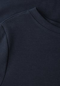 Tissu bleu marine foncé avec un gros plan sur un col rond et une couture d'épaule d'un vêtement, montrant la texture tricotée et les détails de couture.