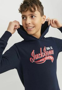 Sudadera con capucha de color azul marino en tejido suave, con un gran diseño gráfico en rojo y blanco que dice "Jack & Jones" en la parte frontal.