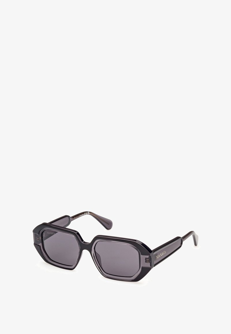 Schwarze, übergroße Sonnenbrille mit achteckiger Form, dunkelgrauen Gläsern, dicken Rahmen und seitlichem Branding. Glattes Kunststoffmaterial.