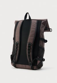 Σκούρο καφέ σακίδιο με επενδυμένη μαύρη δίχτυ πλάτη, ρυθμιζόμενους ιμάντες ώμου, πλαϊνή τσέπη από δίχτυ και επάνω χερούλι πάνω σε απλό φόντο.