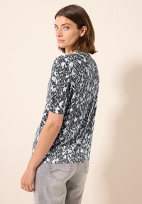 Top de manga corta en un patrón abstracto en gris y negro, con escote redondo, tejido suave, corte holgado, combinado con jeans gris claro.
