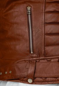 Giacca in pelle marrone con una cerniera argentata, texture trapuntata e dettagli con bottoni a pressione all'orlo. Cuciture decorative lungo i lati.