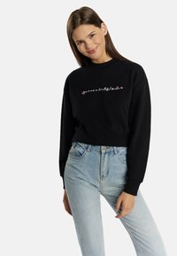 Fekete crop sweatshirt rózsaszín hímzett szöveggel, világoskék, magas derekú farmernadrággal párosítva. Simává textúra és laza szabás.