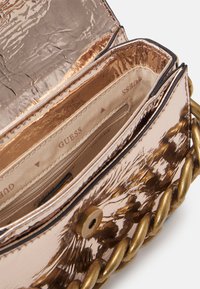 Borsa metallic rose gold con superficie testurizzata, dotata di una grande tracolla a catena e foderatura interna con motivo. Chiusura a flap superiore con snap.