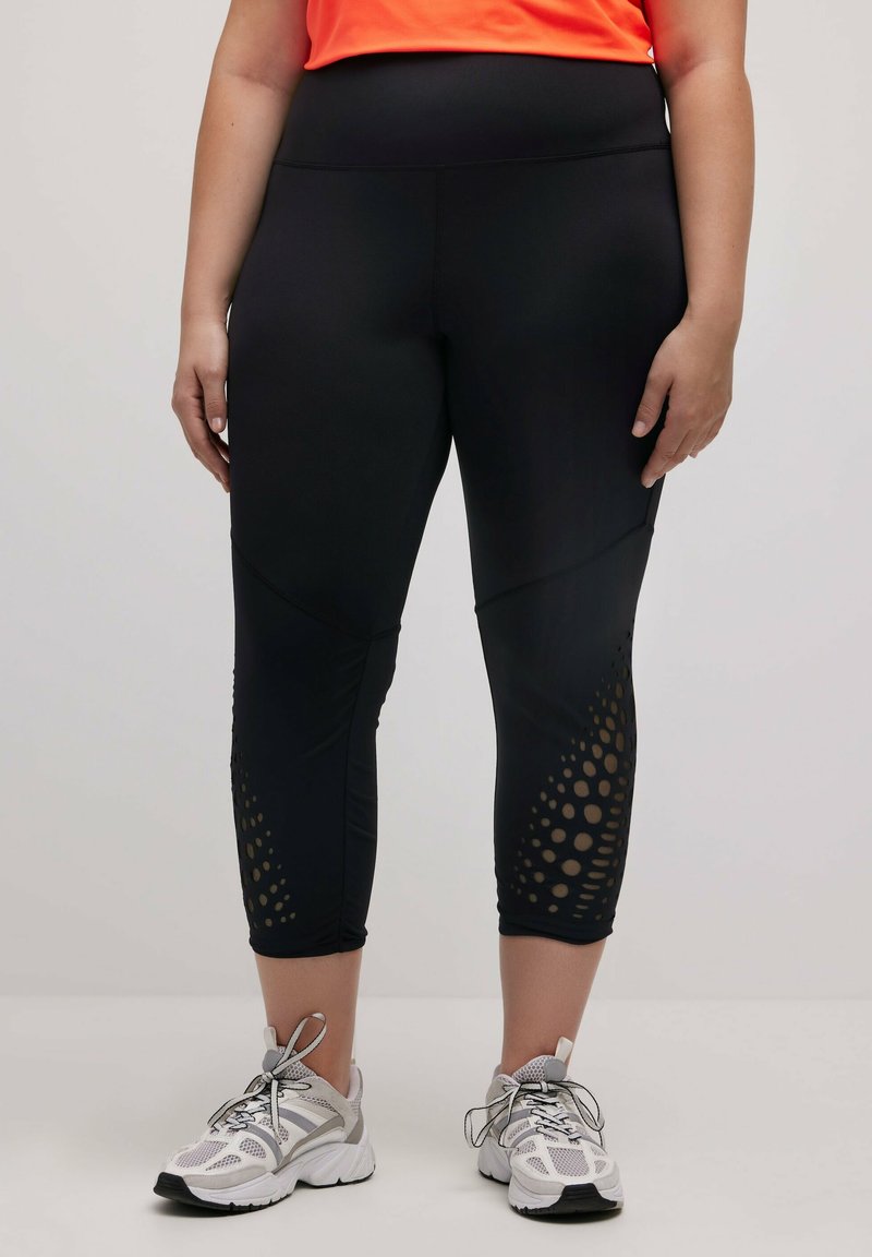 Zwarte leggings met een hoge tailleband, voorzien van geperforeerde accenten bij de zoom en een gladde, rekbare textuur. Draag ze met sportieve schoenen.