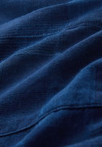 Tessuto blu navy con una texture liscia, caratterizzato da un motivo a quadretti sottile e dettagli di cuciture fini. Materiale leggero e flessibile.