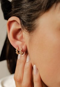 Orecchini a cerchio in oro con decorazioni floreali, adornati con piccole gemme trasparenti e color ambra, mostrati sull'orecchio di un modello.