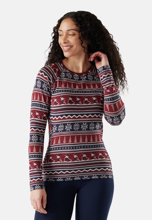 Langärmliges, tailliertes Oberteil in Marineblau und Rot mit einem festlichen Muster aus Schneeflocken, Bäumen und Skifahrern. Gefertigt aus einem weichen, elastischen Material.