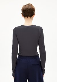 Langärmliges, enganliegendes Oberteil aus dunkelgrauem Stoff. Verfügt über einen Rundhalsausschnitt und eine glatte Textur. Kombiniert mit marineblauen Jogginghosen mit elastischem Bund und einer Gesäßtasche.