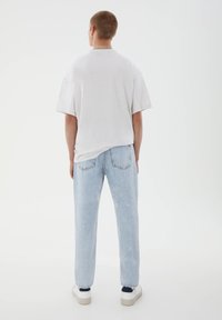 Bílé oversized tričko s volným střihem, doplněné světle modrými džíny s rovnými nohavicemi a bílými teniskami. Jednoduchý a minimalistický design.