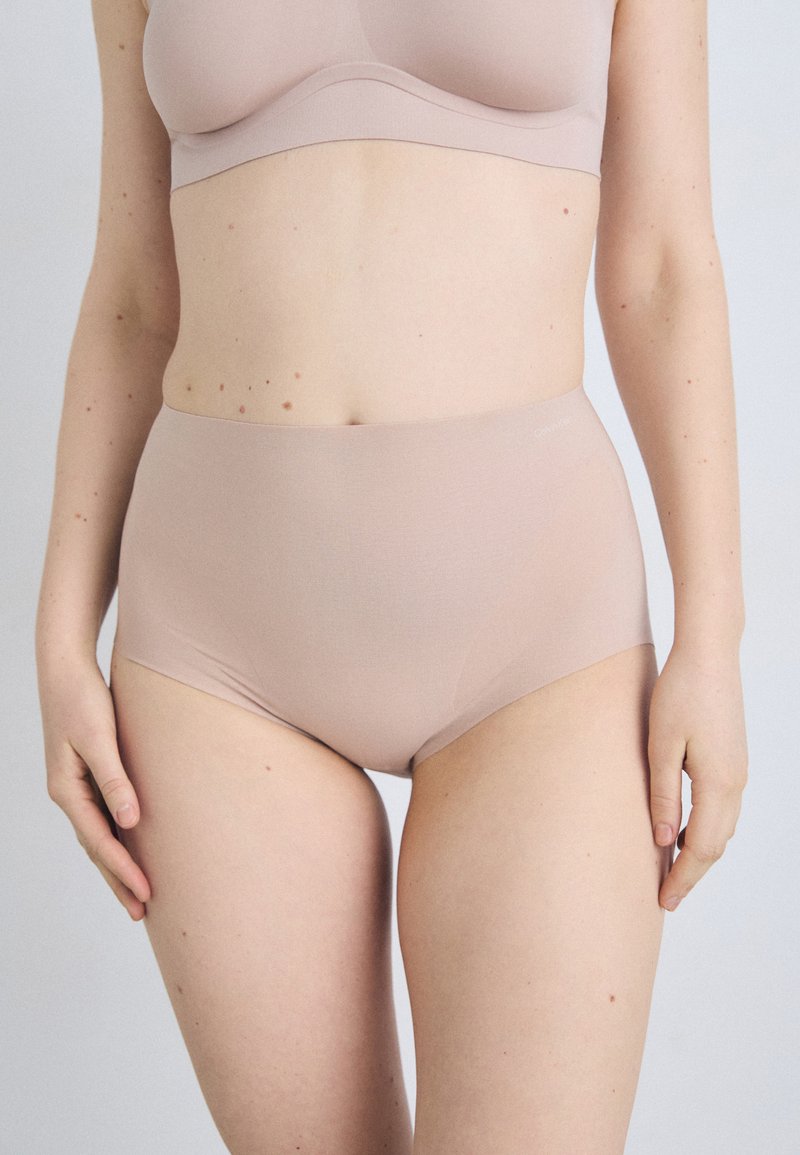Beige høytalere truser laget av glatt stoff, med sømløst design og en komfortabel elastisk midjebånd, minimal detaljering.