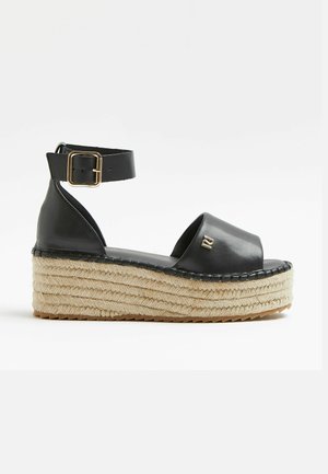 Czarna platformowa sandałka ze skóry z paskiem wokół kostki, koturnem owiniętym jutą, gładkim wykończeniem i złotym akcentem po bokach.