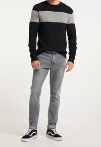 Schwarzer und grauer gestreifter Pullover mit geripptem Stoff, kombiniert mit hellgrauen Jeans und schwarzen Vans-Schuhen mit weißen Akzenten.