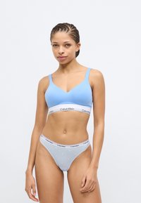 Ανοιχτό μπλε μπουστάκι με ντεκολτέ σε σχήμα V, λευκή ταινία με το λογότυπο "Calvin Klein". Αντίστοιχο ανοιχτό μπλε μπικίνι με αστέρια και ταινία με λογότυπο.