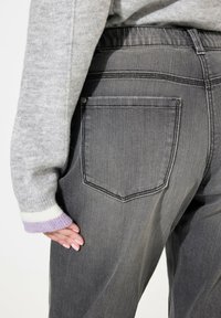Pantalon en denim gris à coupe slim, avec une poche arrière, associé à un pull gris clair avec des rayures blanches et lavande sur les poignets.