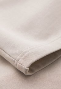 Gros plan d'une manche en tissu beige avec des coutures visibles et un bord replié, montrant une texture douce en maille et des détails de couture.