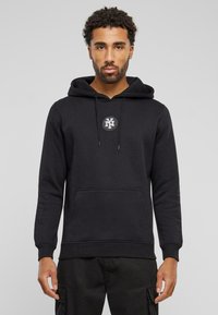 Zwarte hoodie van een katoenmix met een buidelzak, een capuchon met trekkoord en een ronde logo op de borst. Heeft ribgebreide manchetten en zoom.