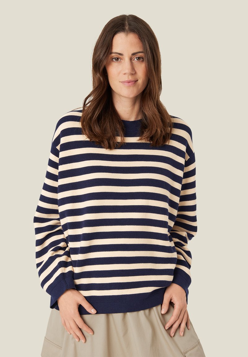 Gestreifter Pullover in Marineblau und Creme mit lockerer Passform, geripptem Halsausschnitt und Bündchen sowie weichem Strickoberfläche. Kombiniert mit einem beigen Rock.