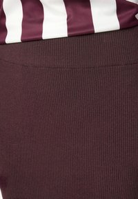 Bordo ribota svārku ar pieguļošu jostasvietu, ar teksturētu virsmu un gludu apdari, papildinātu ar augšējo daļu ar baltām svītrām.