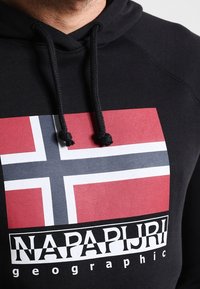 Černá mikina s kapucí s ústředním motivem norské vlajky v červené, bílé a modré barvě. Obsahuje šňůrky na stažení a nápis "NAPAPIJRI".