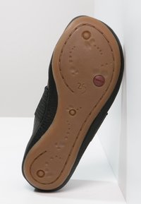 Sohle eines schwarzen Kinderschuhs mit brauner Gummisohle, Größe 25, mit kreisförmigen Mustern und einem roten "Camper"-Logo.