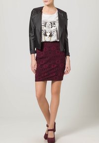 Chaqueta de cuero negra, camiseta blanca con un gráfico de tigre, falda burdeos con estampado y tacones burdeos a juego con un detalle de hebilla.