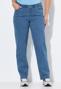 Pantalones de mezclilla azul con un diseño de pierna recta, cintura elástica y bolsillos frontales. Llevados con zapatillas gris y azul.