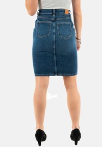 Jupe crayon en denim bleu foncé, avec une taille mi-haute, deux poches arrière et un ourlet net. Le modèle porte des chaussures à talons hauts noires.