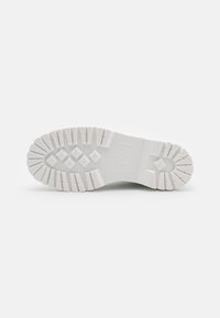 Suela de bota de goma blanca con profundas marcas, patrones de diamante y cruz, y texto en relieve que indica resistencia al aceite, ácidos y deslizamientos.