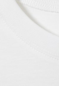 Tissu en coton blanc avec un bord de col côtelé. Texture lisse, présentant un design épuré et simple, sans motifs ni graphiques.