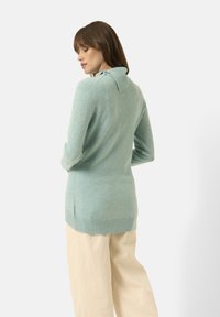 Maglione morbido verde chiaro con colletto ripiegato, maniche lunghe e spacchi laterali, abbinato a pantaloni larghi color crema.