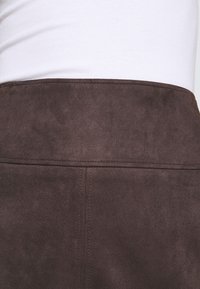 Falda de ante sintético marrón con una textura suave, que presenta una cintura alta y detalles de costura sutiles a lo largo de las costuras.